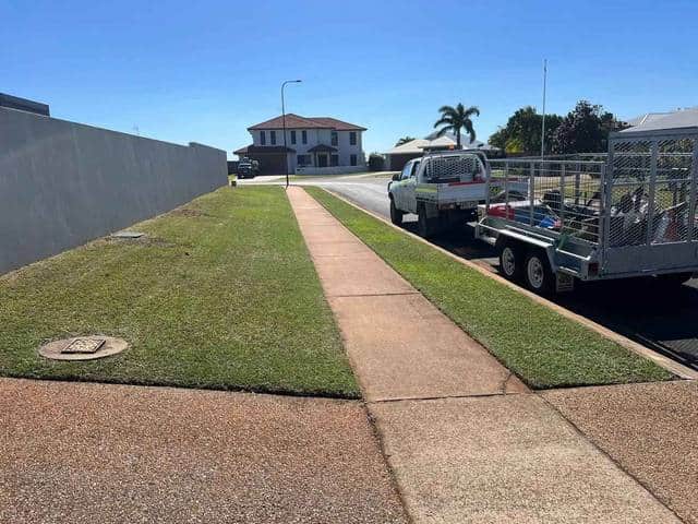 A ute and caged trailer parked at the kerb beside a freshly mown verge