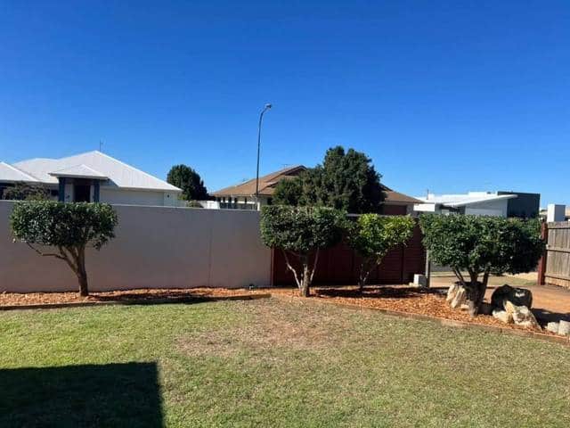 A back lawn cut short with a garden bed along the fence