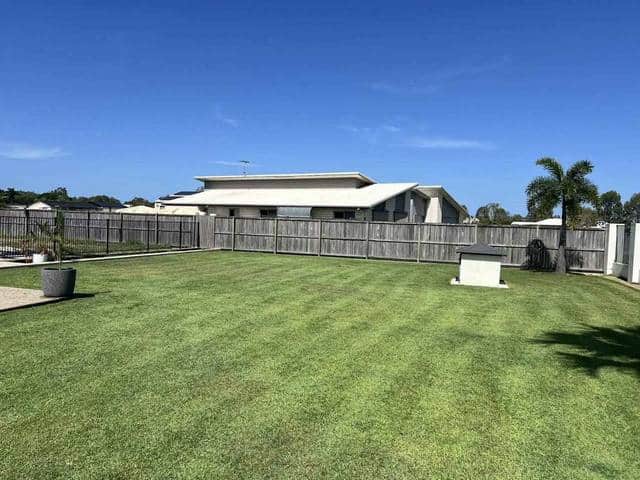 A wide mown lawn in even stripes with palms along the back fence
